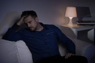 man in shirt sitting on a couch grabbing his head