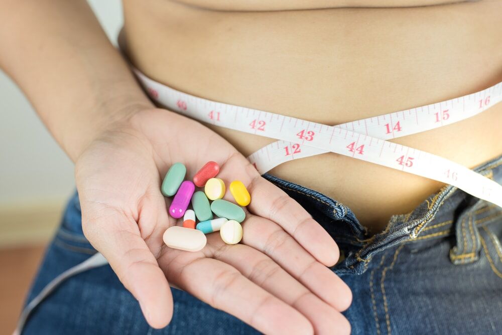 Diet Pill Withdrawal Symbolized by a Person Sitting with a Cloth Tape Measure Around their Waist and a Handful of Pills