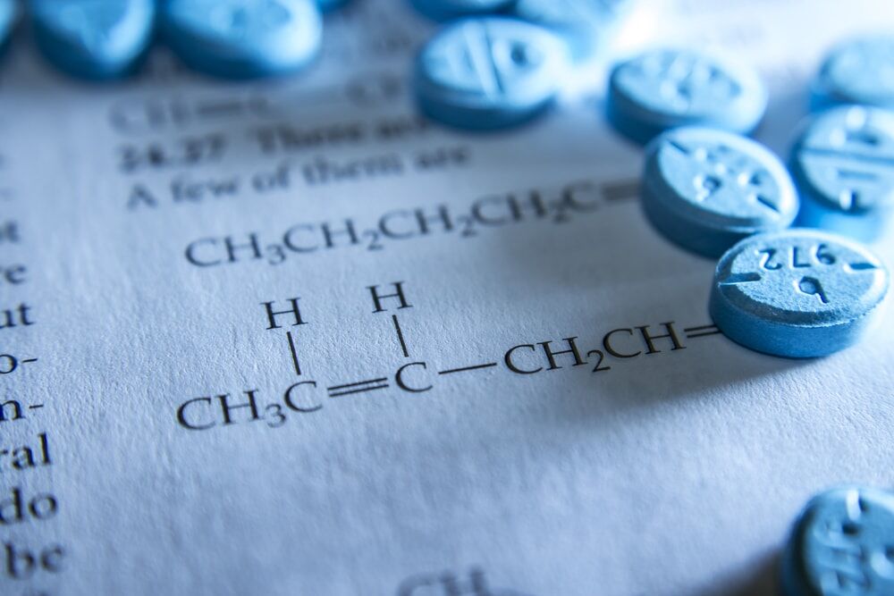 Adderall Withdrawal Symbolized by Blue Pills Scattered on a Piece of Paper with Chemical Formulas Printed on it