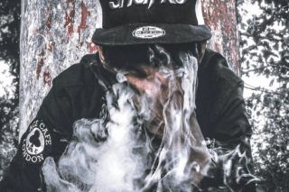 man wearing black Sharks cap and jacket exhaling white smoke