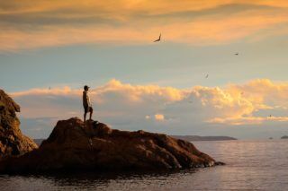 Silhouette of Person Standing on Rock during Sunset